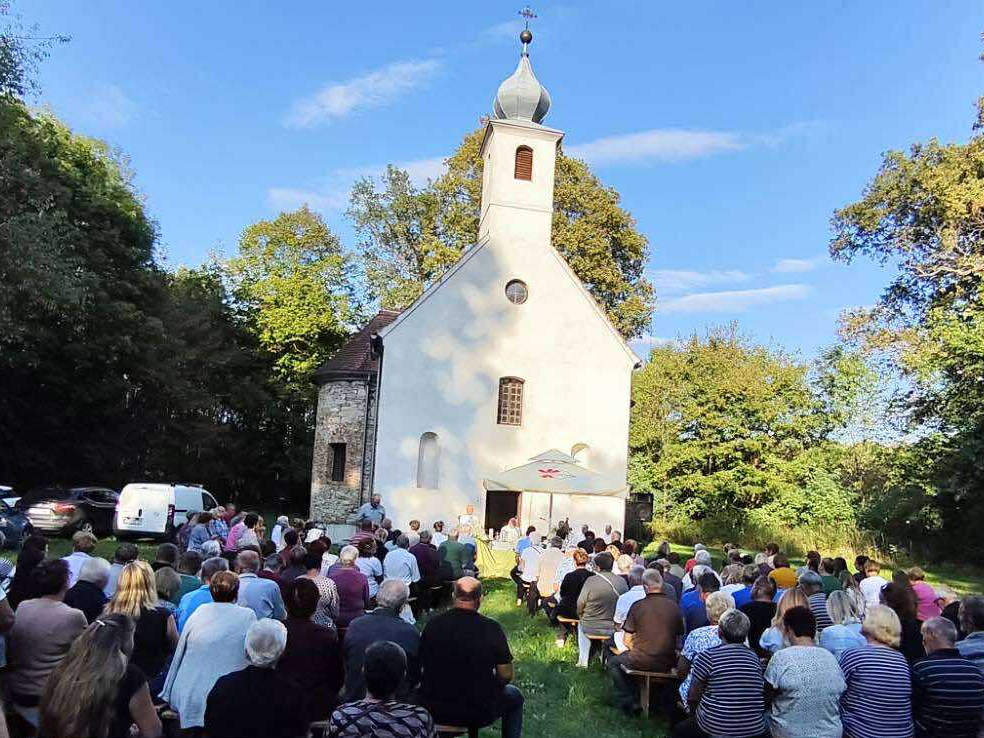 Kapela i mauzolej obitelji Drašković u šumi Križančiji — bijela kapela s lukovičastim tornjem, vjernici sjede na klupama na otvorenom za vrijeme proštenja Imena Marijina.
